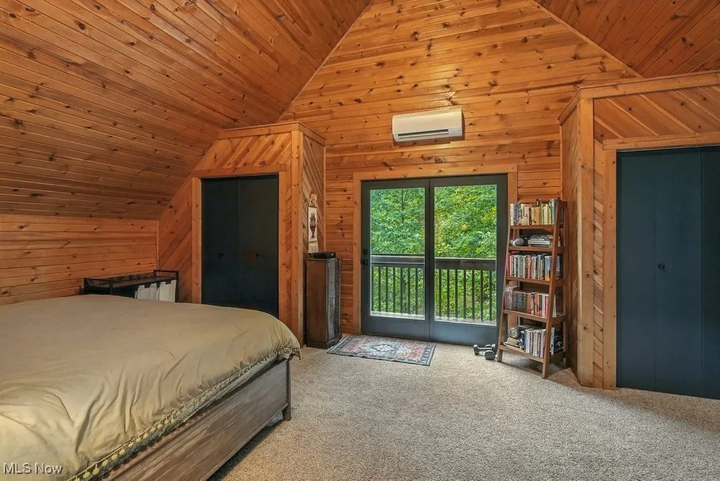 Carpeted bedroom featuring wooden walls, access to exterior, a wall mounted air conditioner, wooden ceiling, and high vaulted ceiling
