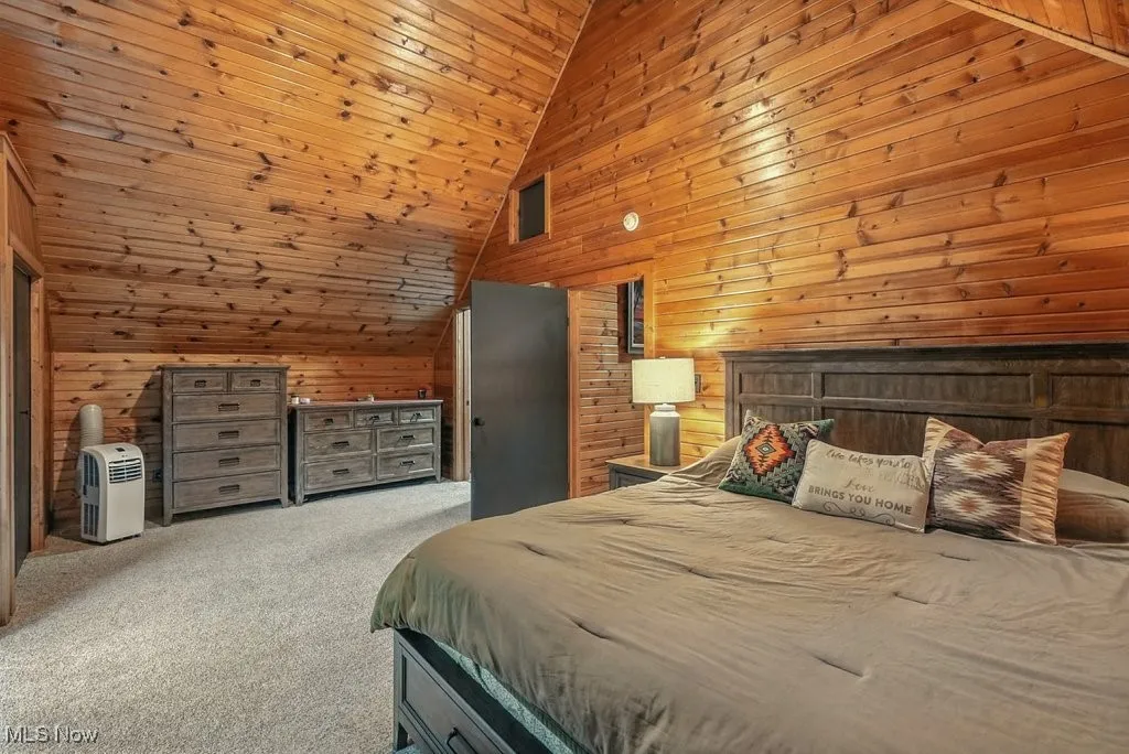 Carpeted bedroom with wooden walls, wooden ceiling, and high vaulted ceiling