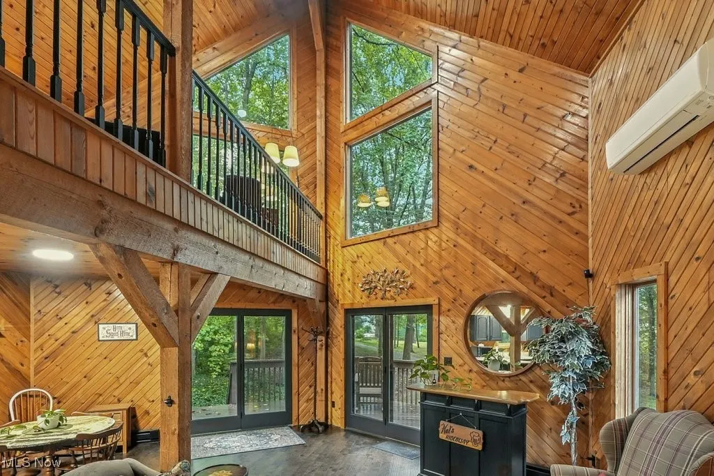 Living room with high vaulted ceiling, wood walls, an AC wall unit, and french doors