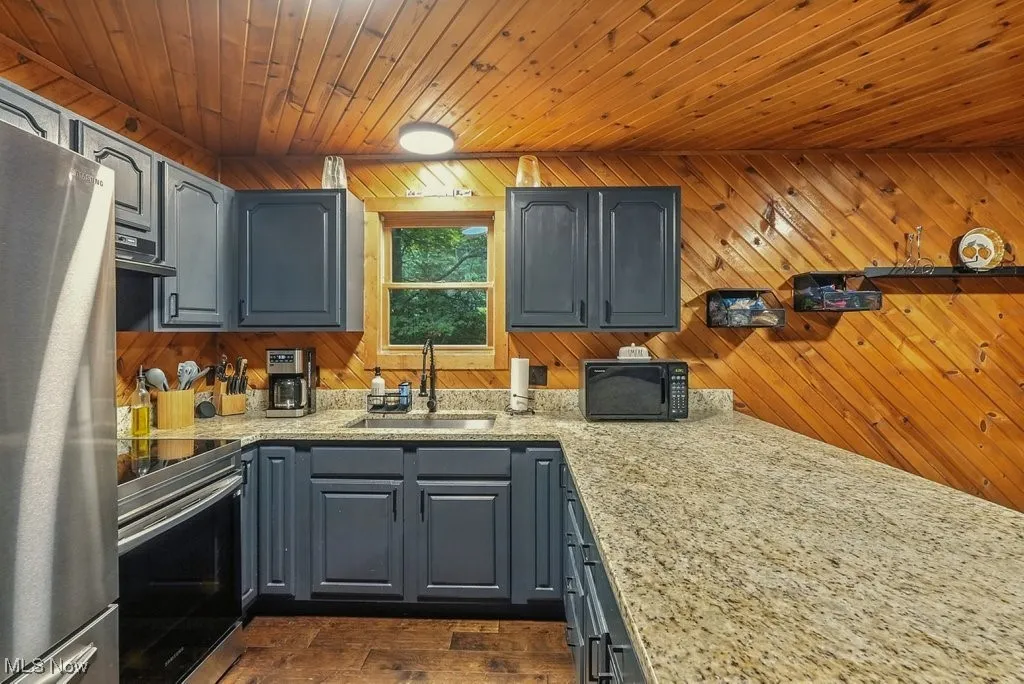 Kitchen featuring appliances with stainless steel finishes, gray cabinetry, wooden ceiling, light stone counters, and dark wood-style floors