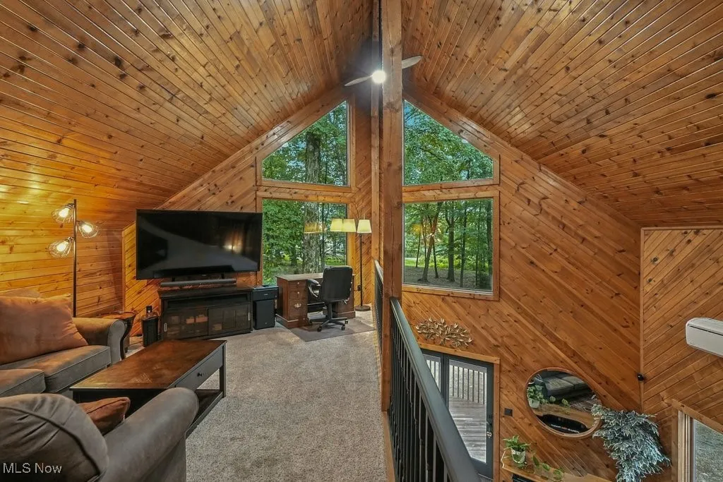 Carpeted living area featuring wooden walls, high vaulted ceiling, and wooden ceiling