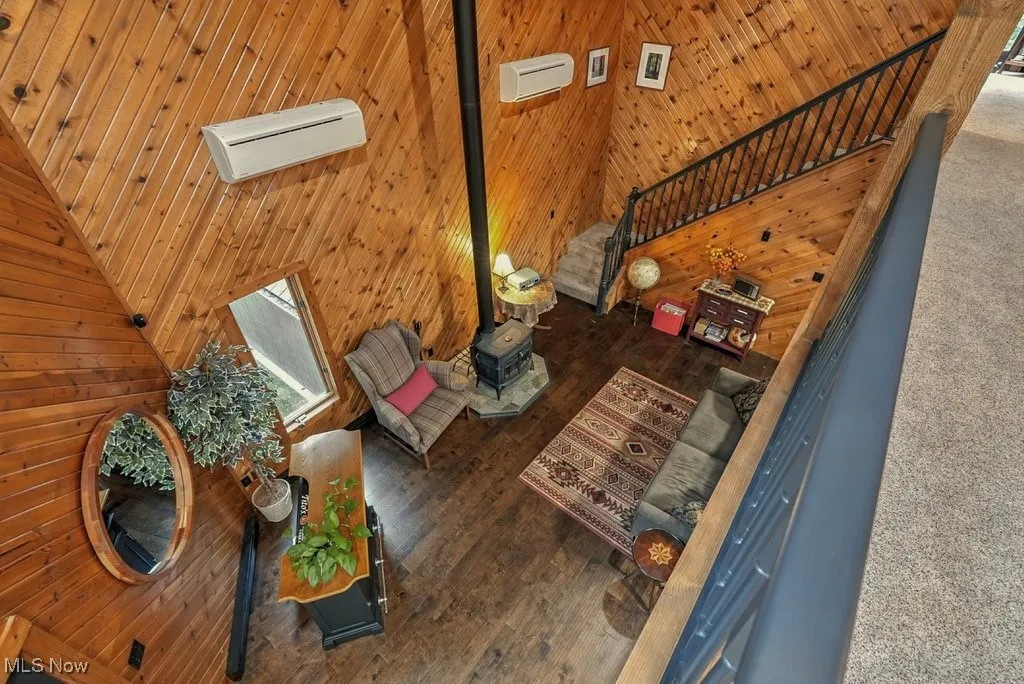 Living area featuring high vaulted ceiling, wood walls, a wood stove, and wood finished floors
