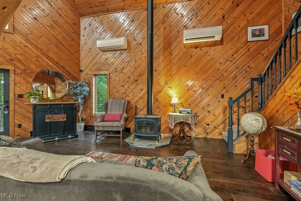 Living room featuring a high ceiling, stairs, a wood stove, dark wood-type flooring, and wooden walls