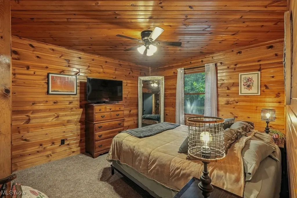 Carpeted bedroom with wooden walls, wood ceiling, and a ceiling fan