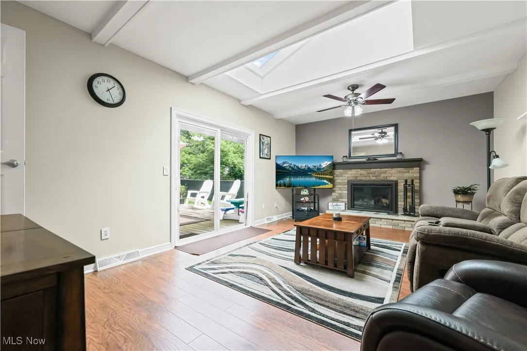 Living room featuring a skylight, beam ceiling, wood finished floors, and a glass covered fireplace