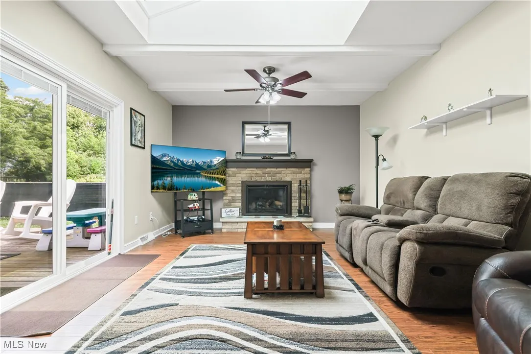 Living room featuring beamed ceiling, wood finished floors, a fireplace, and a ceiling fan