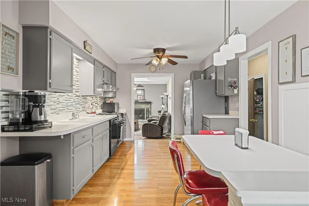 Kitchen with gray cabinets, hanging light fixtures, light countertops, light wood-type flooring, and ceiling fan