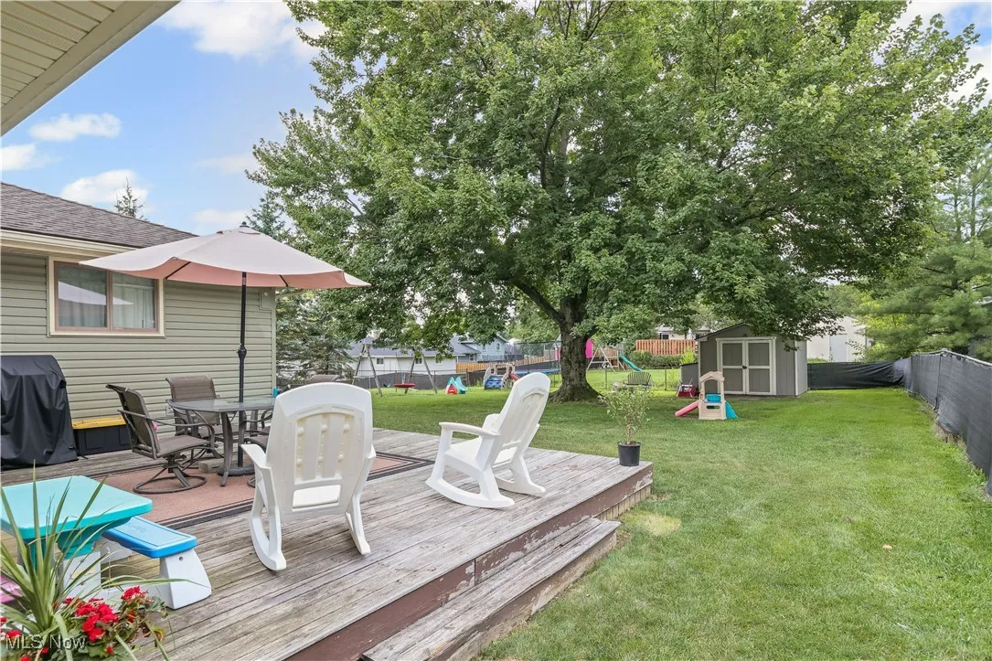 Deck with a playground, a shed, a fenced backyard, outdoor dining area, and a grill