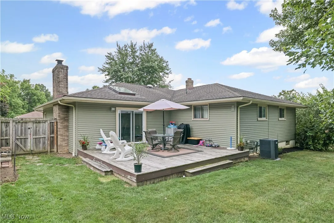 Rear view of house with a wooden deck, a chimney, outdoor dining area, and a shingled roof