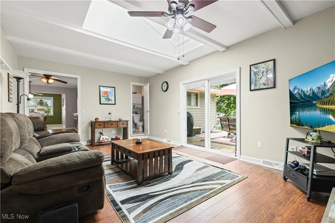 Living room featuring ceiling fan, beamed ceiling, wood finished floors, and healthy amount of natural light