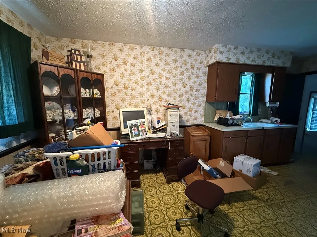 Kitchen featuring a textured ceiling, wallpapered walls, light countertops, and an office area