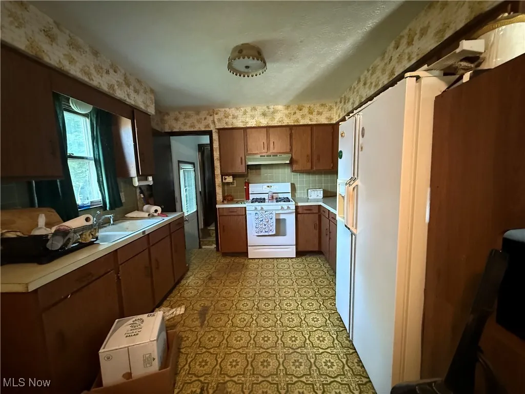Kitchen with light countertops, white range with gas stovetop, tasteful backsplash, light floors, and brown cabinetry