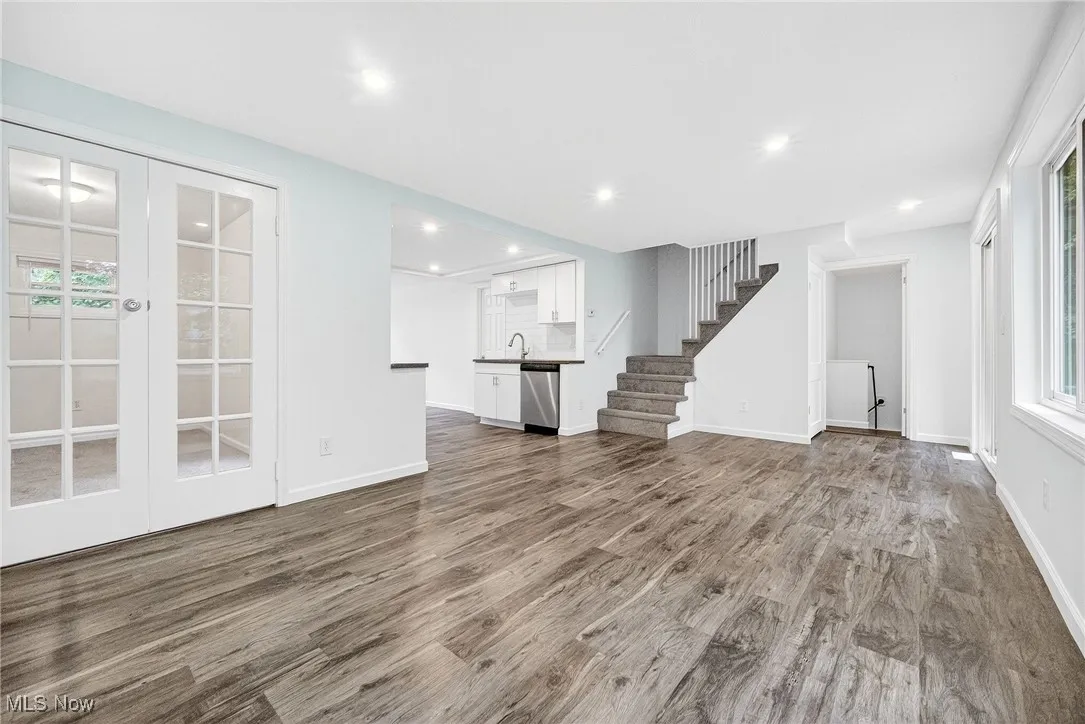 Unfurnished living room with healthy amount of natural light, wood finished floors, stairs, french doors, and recessed lighting