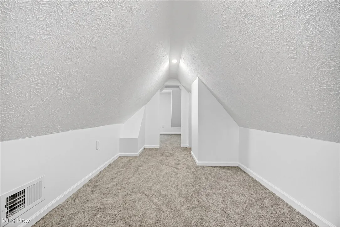 Bonus room with carpet, a textured ceiling, and vaulted ceiling