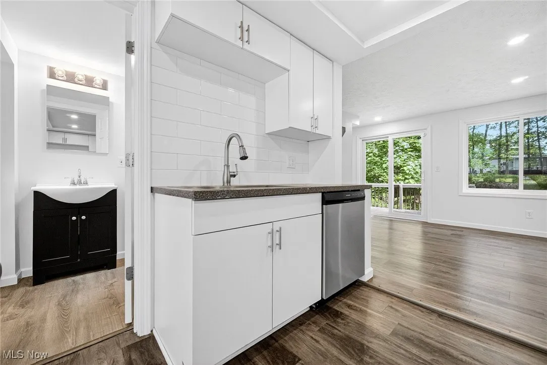 Kitchen featuring white cabinets, stainless steel dishwasher, dark wood-type flooring, recessed lighting, and dark stone counters