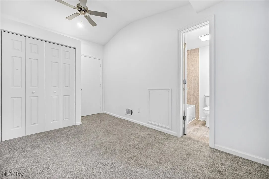 Unfurnished bedroom featuring vaulted ceiling, light carpet, a closet, a ceiling fan, and ensuite bath