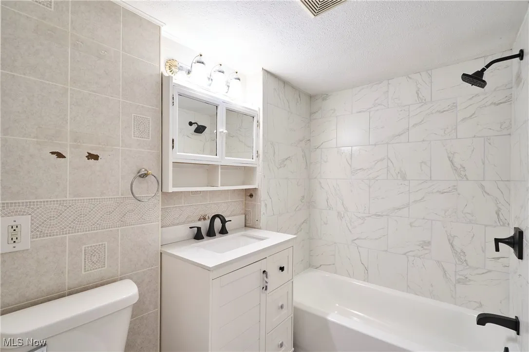 New Bathroom featuring shower / bath combination, tile walls, vanity, new faucets and lighting