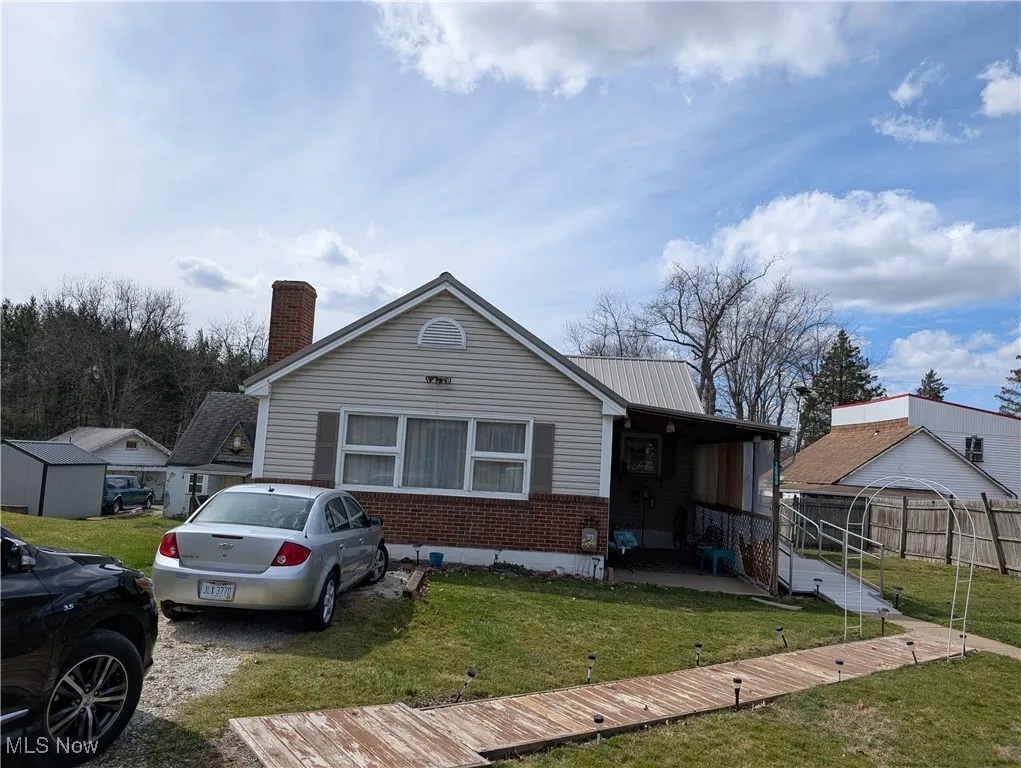 View of front of home featuring a front lawn, brick siding, a chimney, and a metal roof