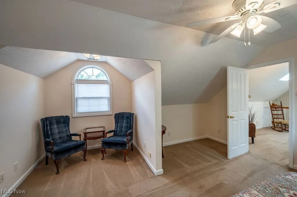 Sitting room with vaulted ceiling, a textured ceiling, light carpet, and ceiling fan