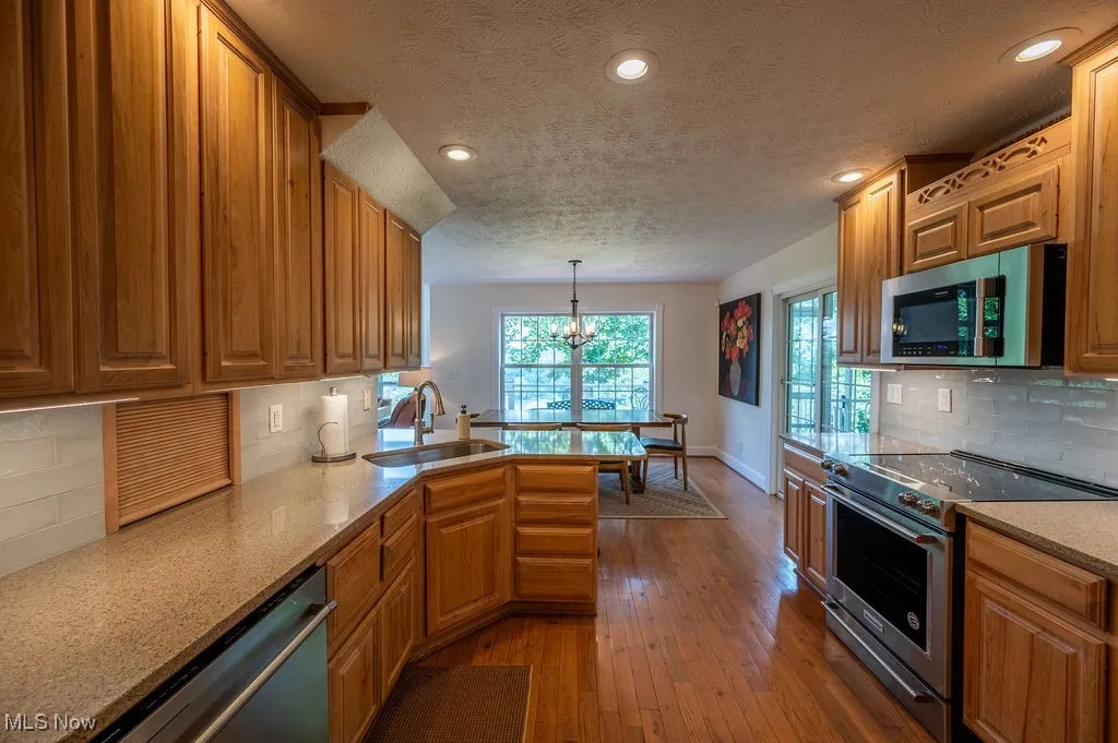 Kitchen featuring decorative backsplash, appliances with stainless steel finishes, hanging light fixtures, light stone countertops, and dark wood finished floors