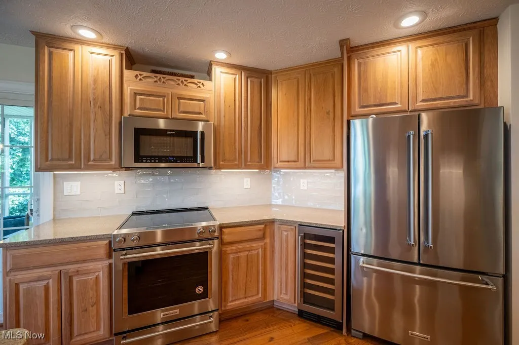 Kitchen featuring stainless steel appliances, light stone countertops, wine cooler, a textured ceiling, and backsplash