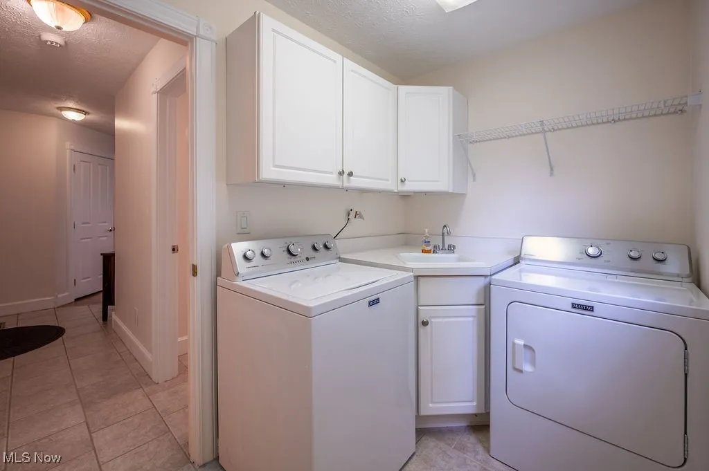 Laundry area featuring washer and clothes dryer, a textured ceiling, cabinet space, and light tile patterned floors