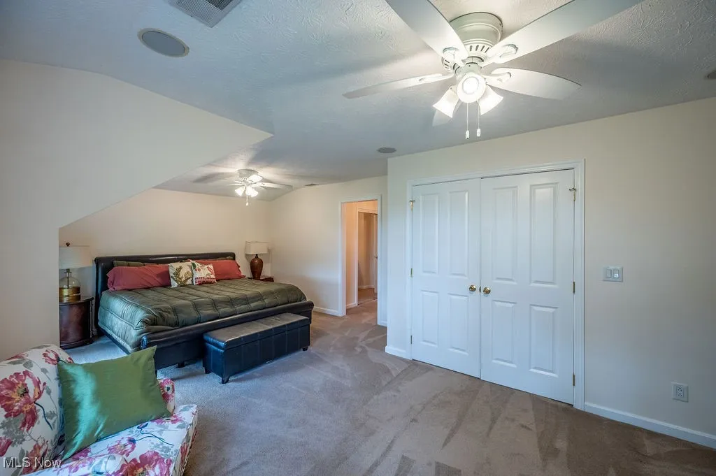 Carpeted bedroom with ceiling fan, a textured ceiling, vaulted ceiling, and a closet