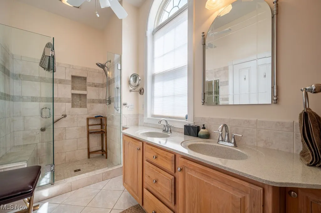 Full bathroom featuring double vanity, a shower stall, light tile patterned flooring, and ceiling fan