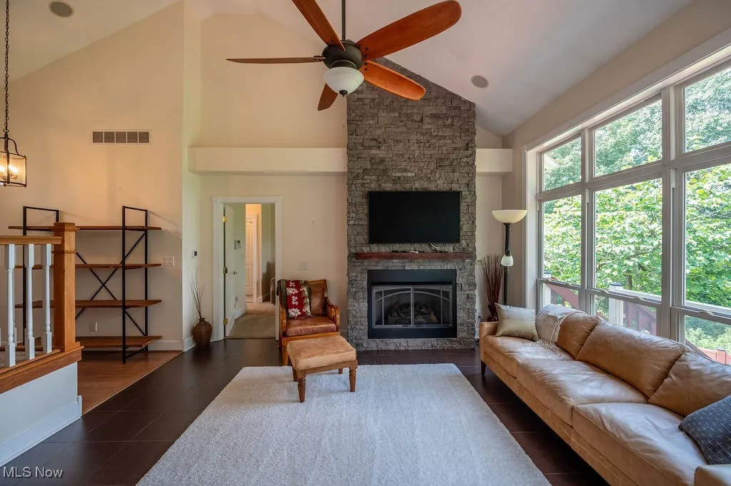 Living area featuring high vaulted ceiling, a fireplace, ceiling fan, and dark tile patterned floors