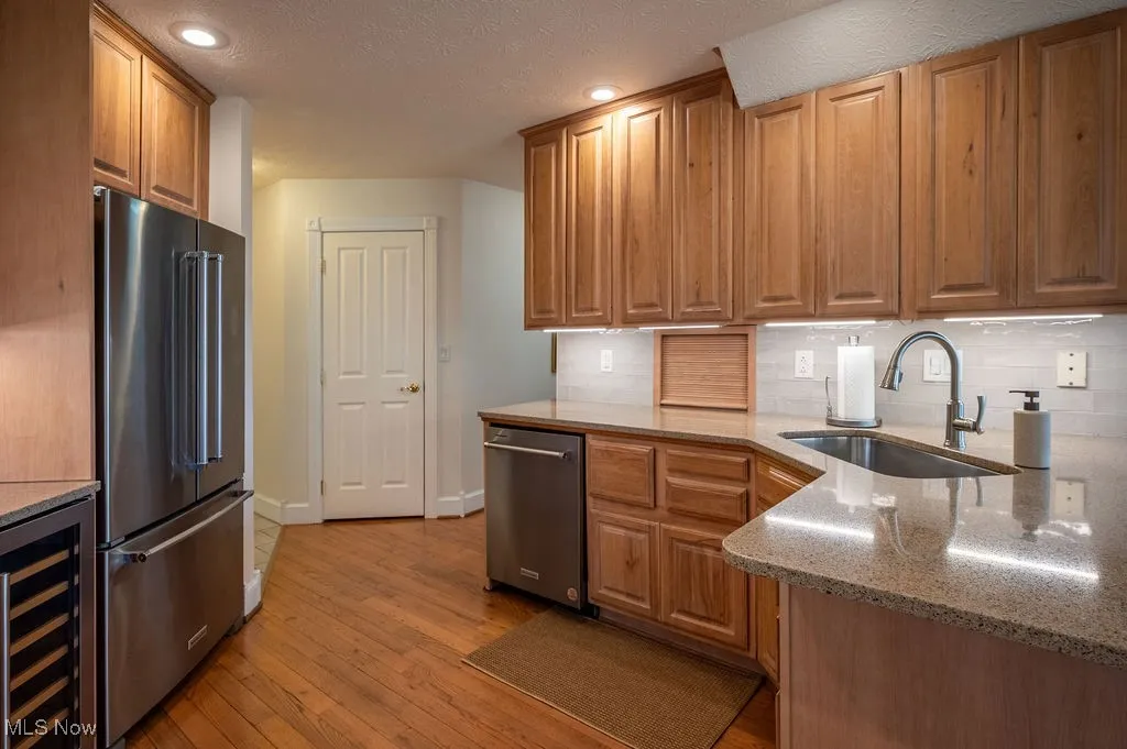 Kitchen with light stone countertops, stainless steel appliances, wine cooler, light wood finished floors, and decorative backsplash