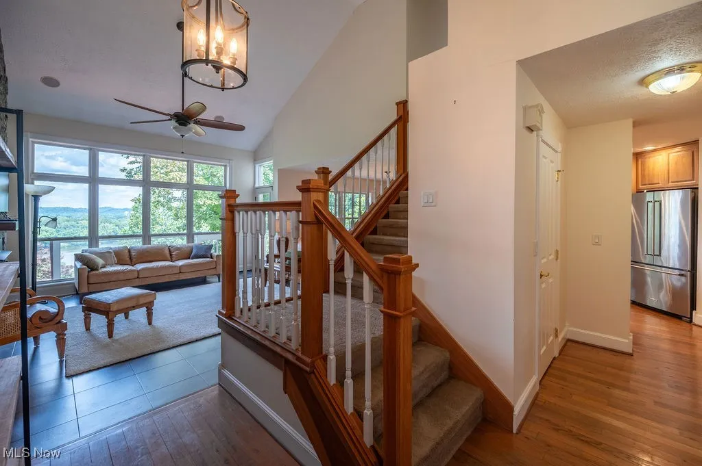 Staircase featuring high vaulted ceiling, hardwood / wood-style flooring, ceiling fan, a textured ceiling, and a chandelier