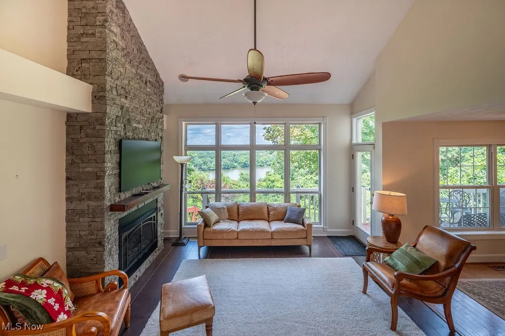 Living area with healthy amount of natural light, high vaulted ceiling, wood finished floors, a stone fireplace, and ceiling fan