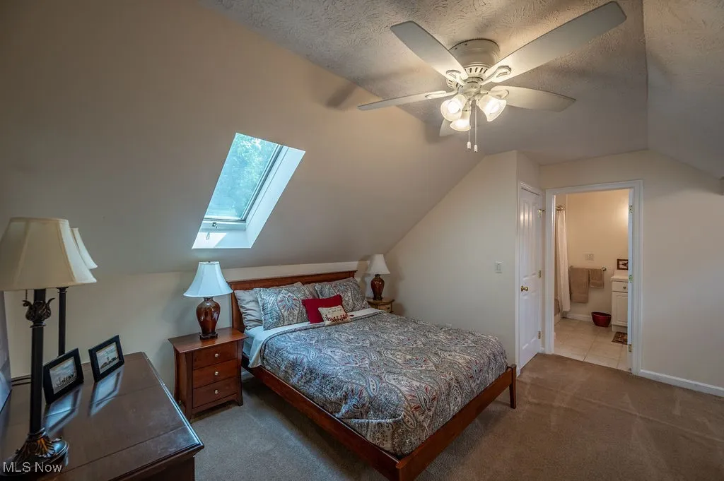 Bedroom featuring vaulted ceiling, ensuite bath, carpet, ceiling fan, and a textured ceiling