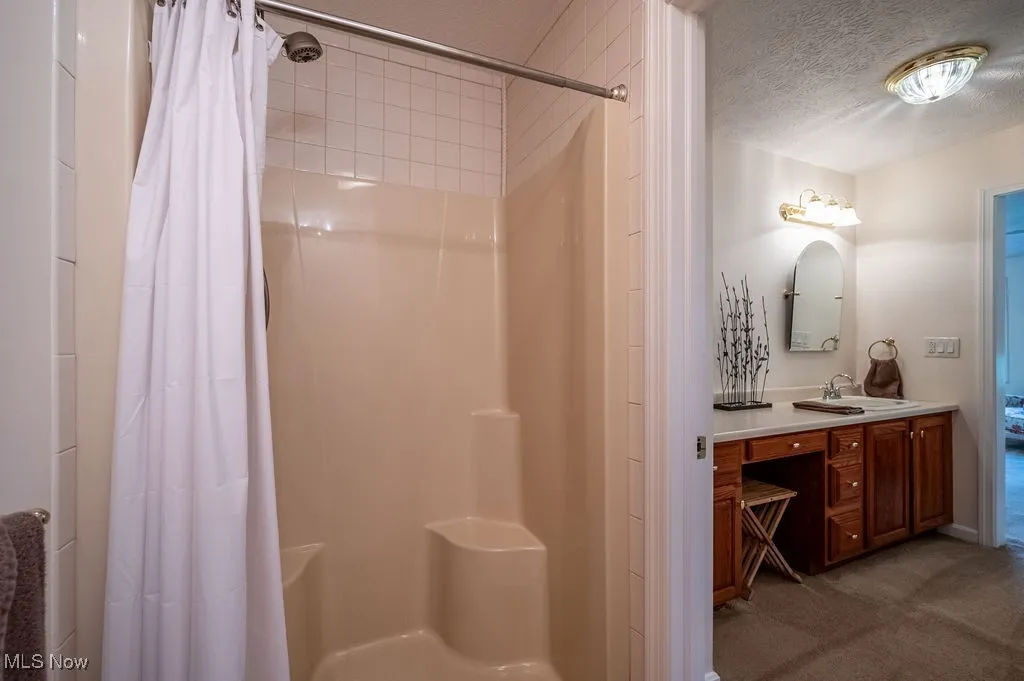 Full bath featuring a textured ceiling, vanity, and a shower stall