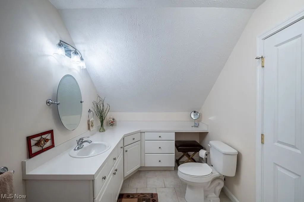 Bathroom with a textured ceiling, light tile patterned floors, vanity, and lofted ceiling
