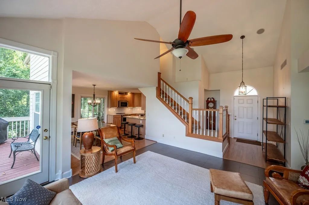 Living room featuring a chandelier, high vaulted ceiling, a ceiling fan, stairs, and dark wood-type flooring