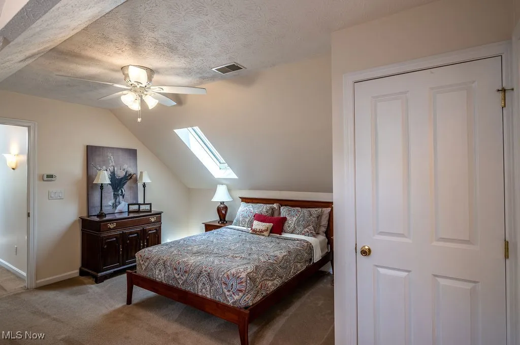 Bedroom featuring lofted ceiling, carpet floors, a skylight, a textured ceiling, and a ceiling fan