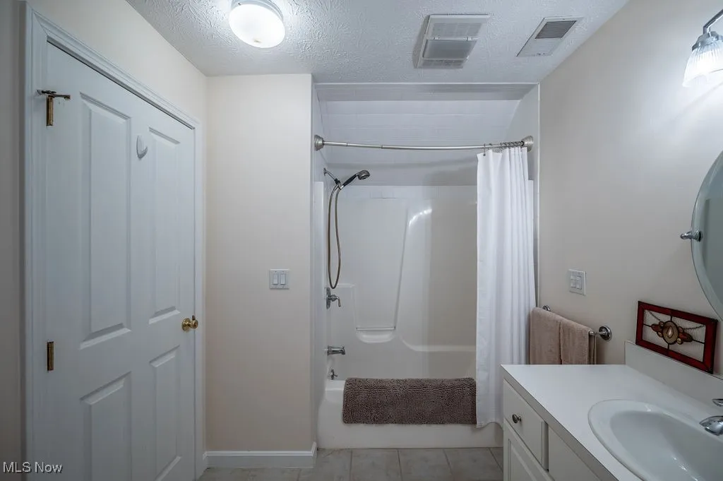 Full bathroom with shower / tub combo with curtain, a textured ceiling, vanity, and light tile patterned flooring