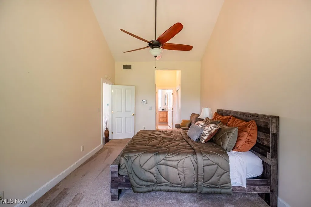 Bedroom with high vaulted ceiling, ensuite bathroom, carpet flooring, and a ceiling fan