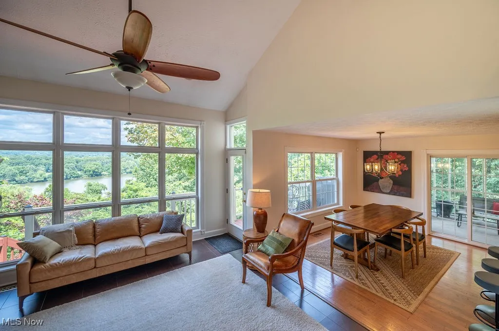Living room with plenty of natural light, wood finished floors, high vaulted ceiling, a water view, and a ceiling fan