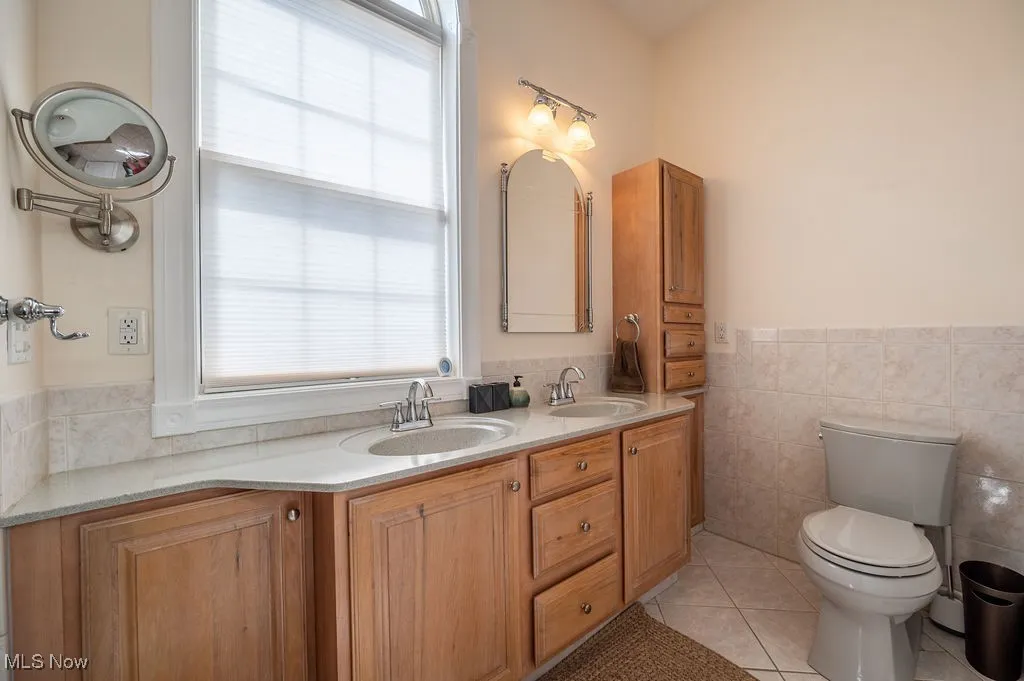 Full bathroom with healthy amount of natural light, light tile patterned floors, tile walls, double vanity, and wainscoting