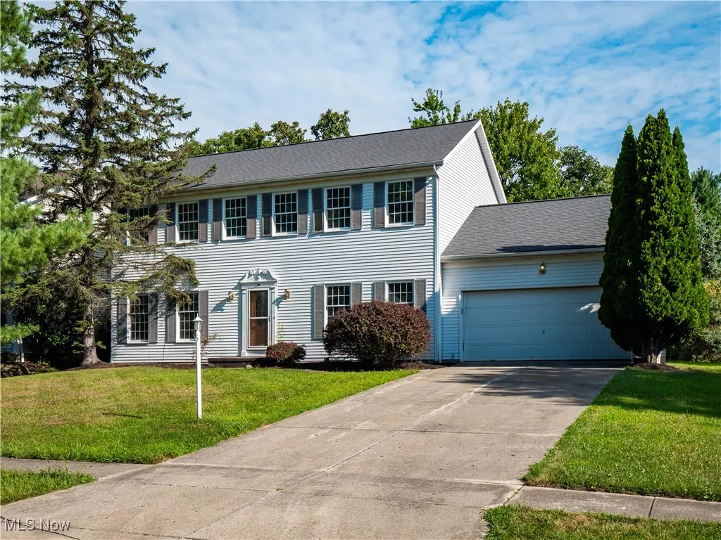 Colonial house featuring an attached garage, concrete driveway, a front lawn, and roof with shingles