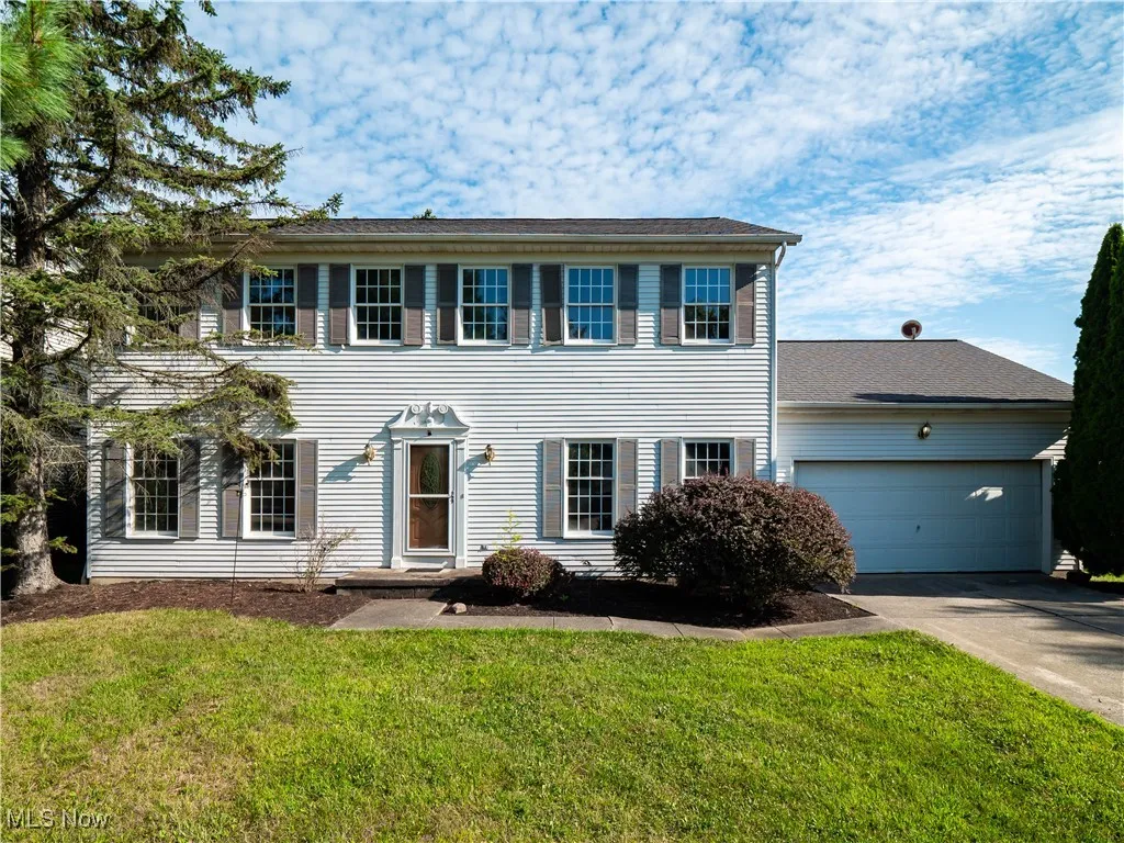 Colonial-style house featuring a garage, concrete driveway, and a front lawn