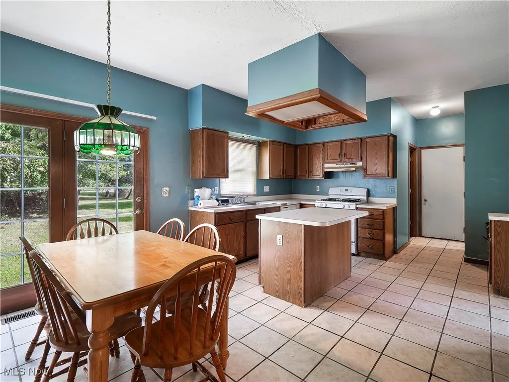 Kitchen with white gas stove, light tile patterned floors, pendant lighting, a center island, and light countertops