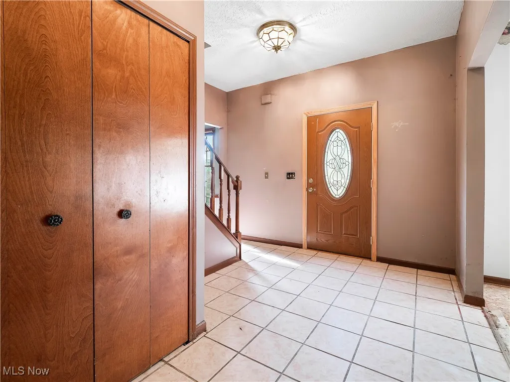 Foyer entrance with light tile patterned floors, stairs, and a textured ceiling