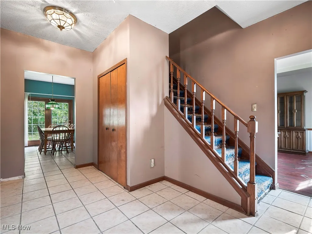 Entryway featuring light tile patterned flooring, a textured ceiling, and stairs