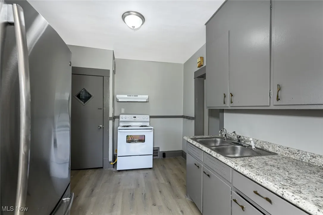 Kitchen featuring gray cabinetry, freestanding refrigerator, white electric range, light wood finished floors, and light countertops