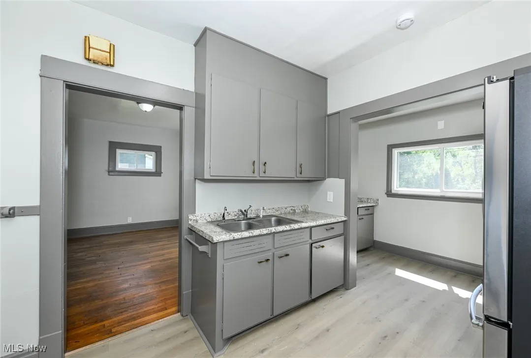 Kitchen with gray cabinetry, light wood-style floors, freestanding refrigerator, light countertops, and healthy amount of natural light