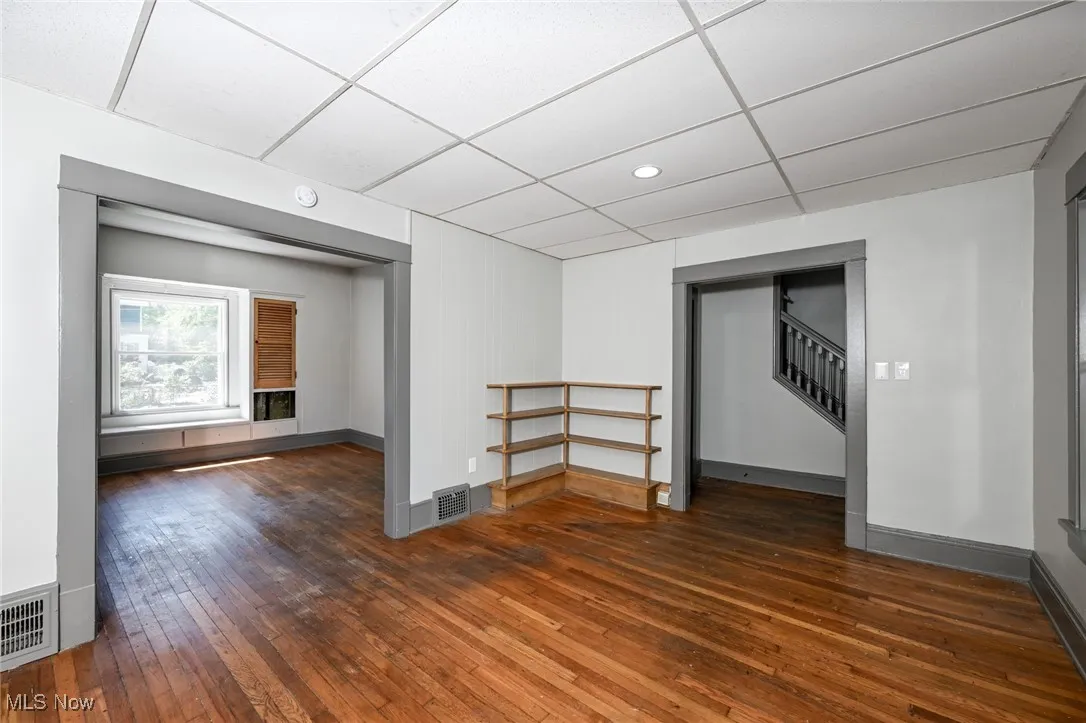 Unfurnished room featuring dark wood-style flooring, a drop ceiling, and stairs