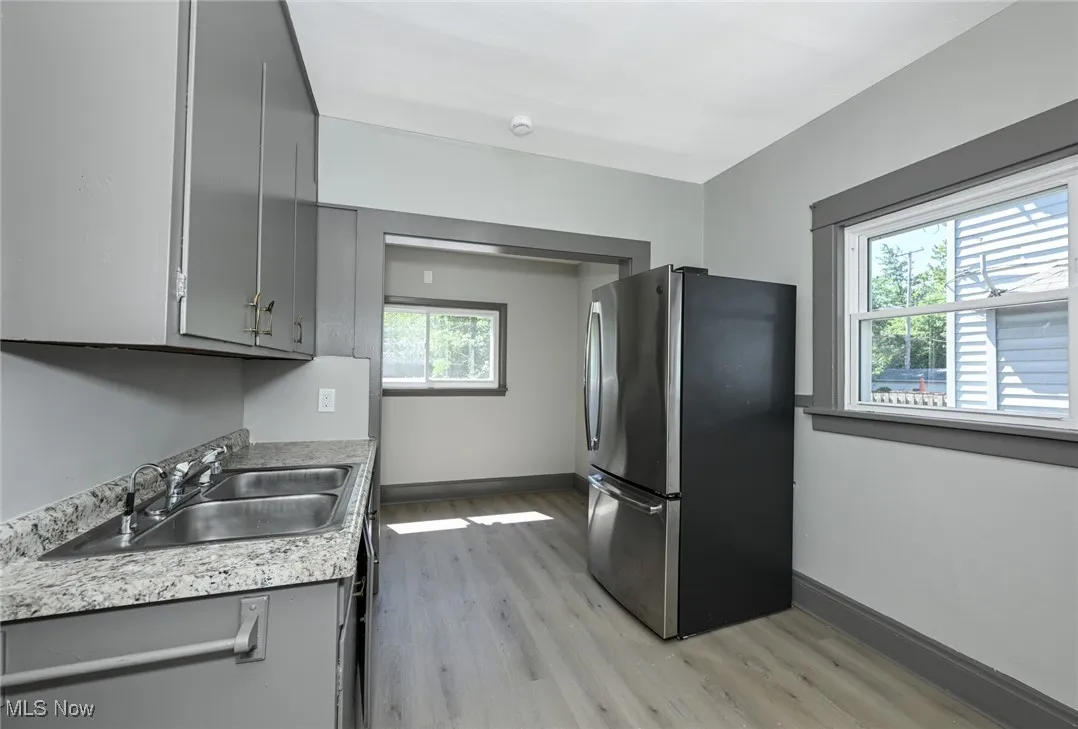 Kitchen with gray cabinetry, freestanding refrigerator, light wood-style flooring, and light countertops